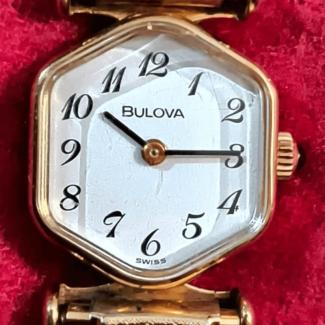 Gold colored watch with a hexagon shaped bezel and white face with stylized Arabic numbers