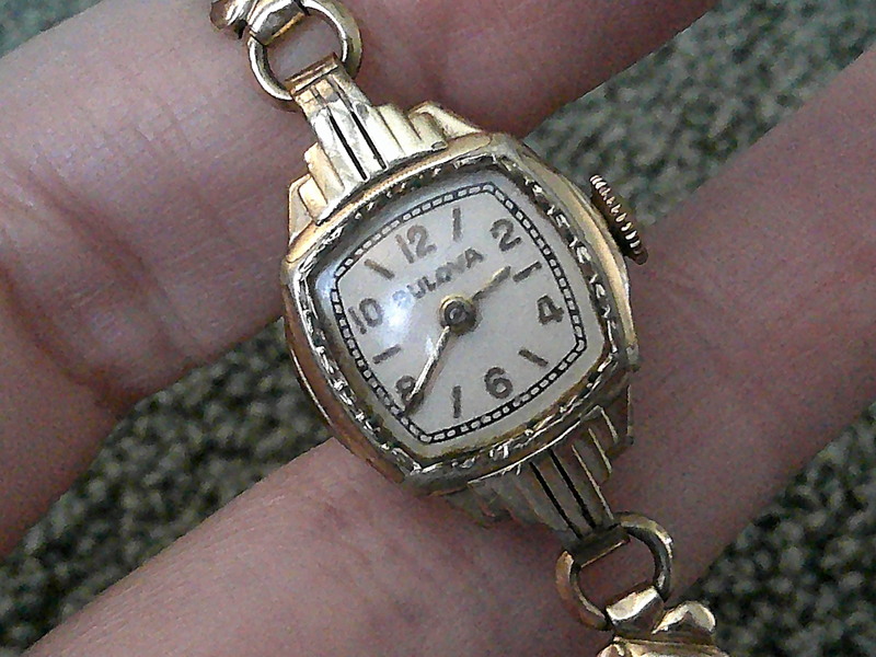 Person holding a goldtone art deco watch at slight left diagonal