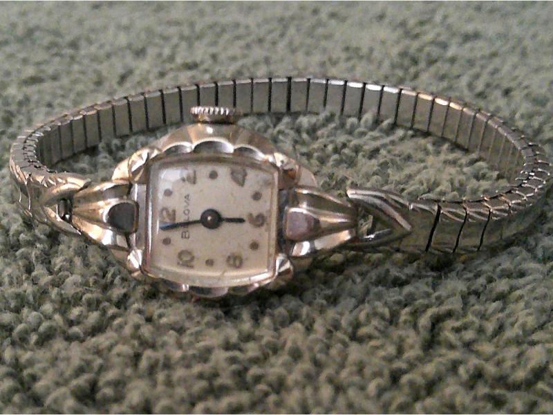 White goldtone midcentuyr watch lying on its side with a stainless steel watch strap