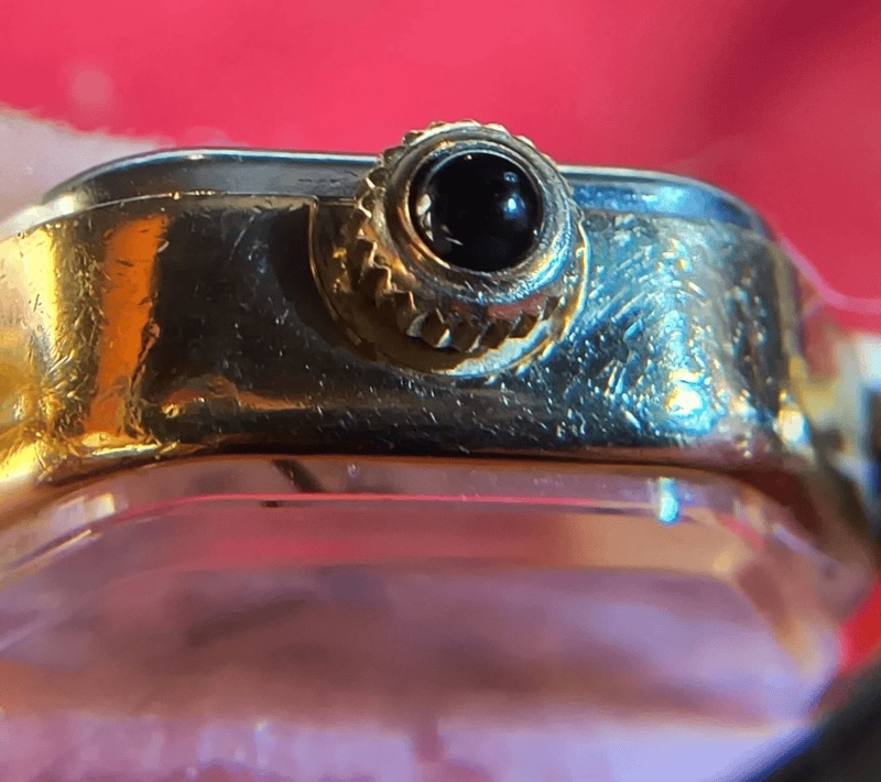 Close-up of winder with a black enamel or gem with radial lines around the gold colored knob.