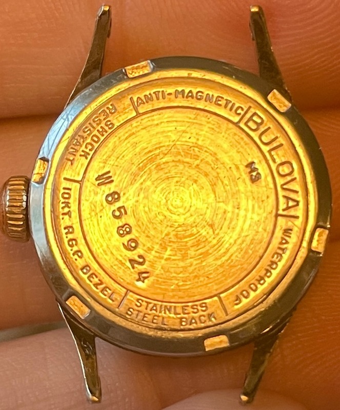 Back of gold watch case with year code and serial number, as well as “shock resistant” “anti-magnetic” “waterprooof” “10kt. R. G. P. Bezel”