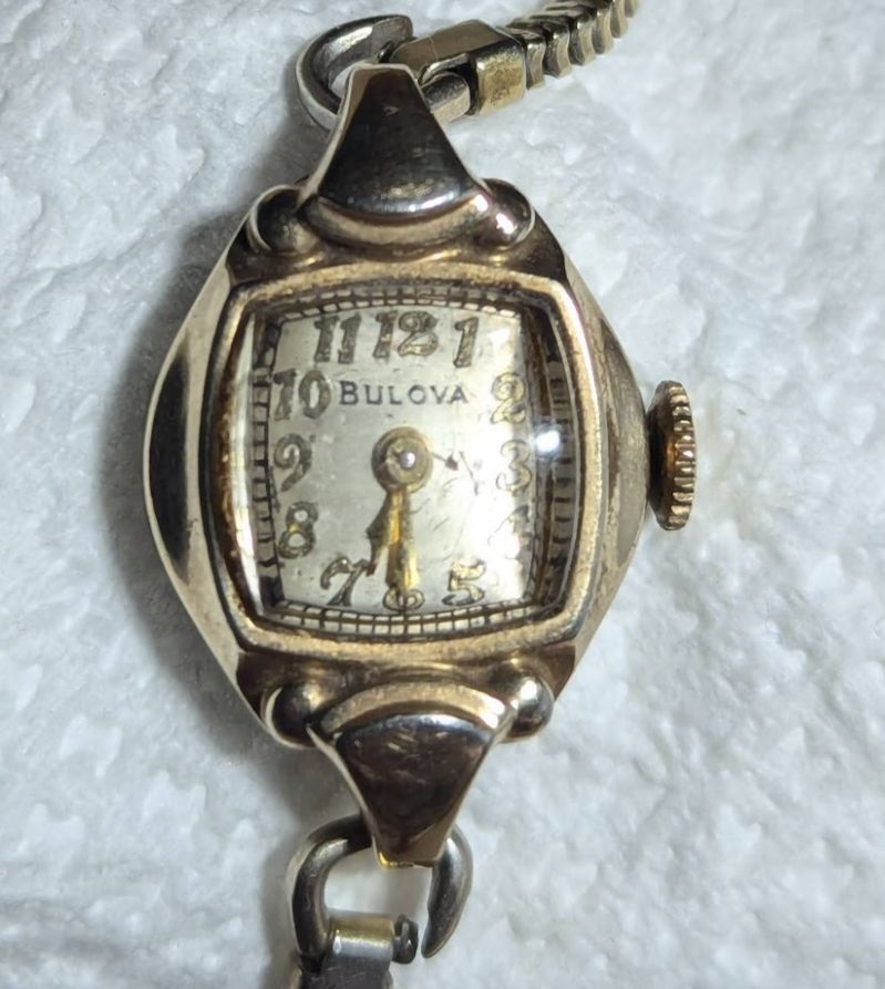 A picture of a Bulova vintage watch with a square dialthat has gold raised digits, gold hands. It has a single lug on the top and bottom that attaches to a gold toned bracelet.
